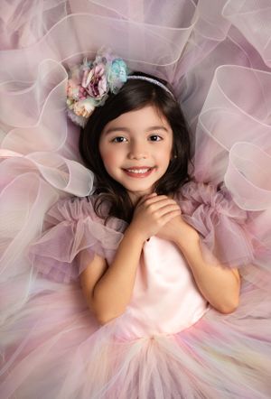 A dreamy portrait in soft pink featuring a tulle dress and floral headpiece with delicate styling.