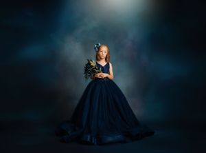 Dramatic portrait in a navy blue ball gown against a moody dark background with spotlight effect.