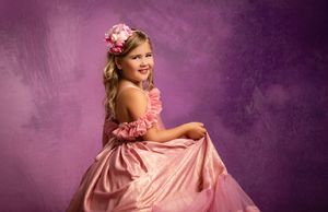 Girl in pink dress twirls and dances in multiple poses against a purple backdrop during a photo shoot session.