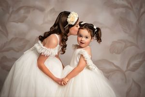 A tender moment between a bride and young child in white dresses against a soft neutral background.