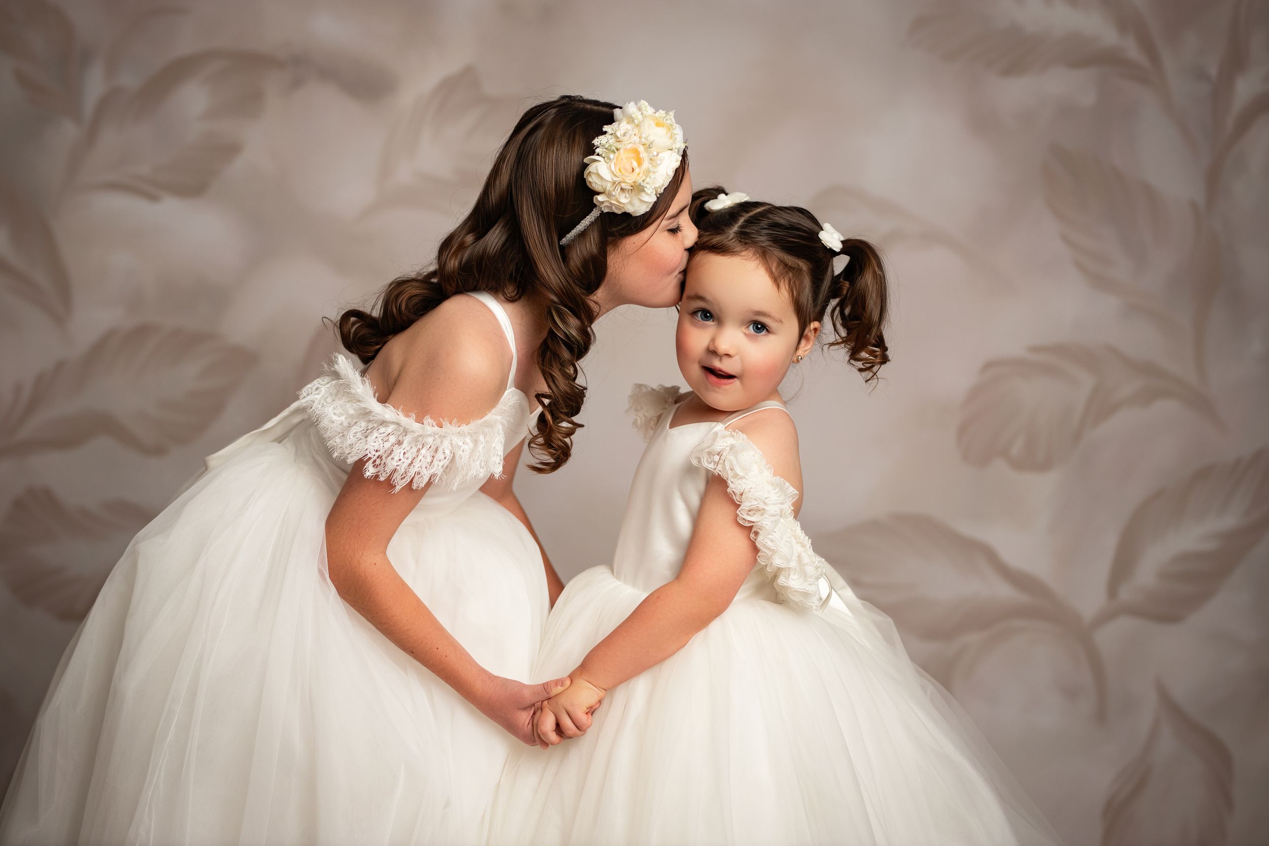 A tender moment between a bride and young child in white dresses against a soft neutral background.