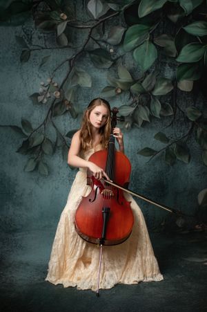 Musician in cream lace dress performs with cello against moody green wall with climbing foliage.  Warrenton VA