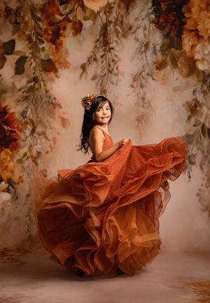 A flowing burnt orange gown twirls dramatically against a backdrop of autumn foliage and dreamy mist.