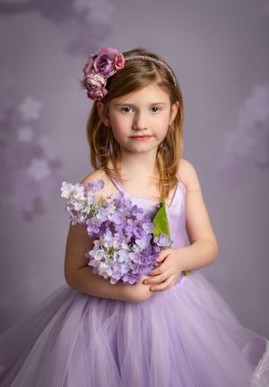 Beautiful portrait in lavender tones featuring a child in a tulle dress holding purple and pink flowers.