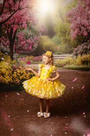 A bright yellow princess dress twirls in a magical garden setting with blooming pink cherry blossoms and golden sunlight.  Warrenton VA