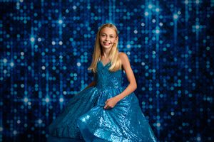 A woman in a sparkly blue ball gown poses and twirls against a glittering blue bokeh background.