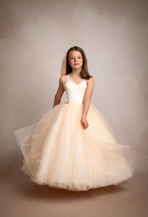 A young dancer in a flowing tulle ballgown poses gracefully against a neutral studio backdrop.
