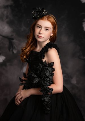 Fine art portrait series featuring dramatic black dress with ruffled details against dark cloudy backdrop in studio setting.