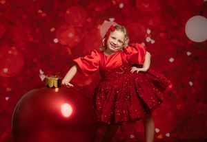 Young child in a red tulle dress twirls against a sparkly crimson holiday backdrop.