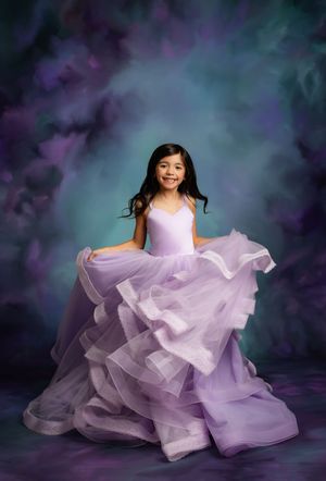 A dreamy portrait of someone in a flowing lavender tulle gown against a dark ethereal background.