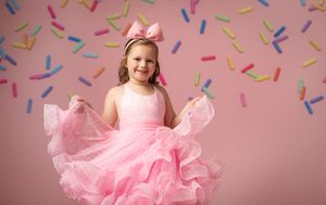 Little girl in pink tulle ballet dress twirls surrounded by floating colorful paper confetti pieces.
