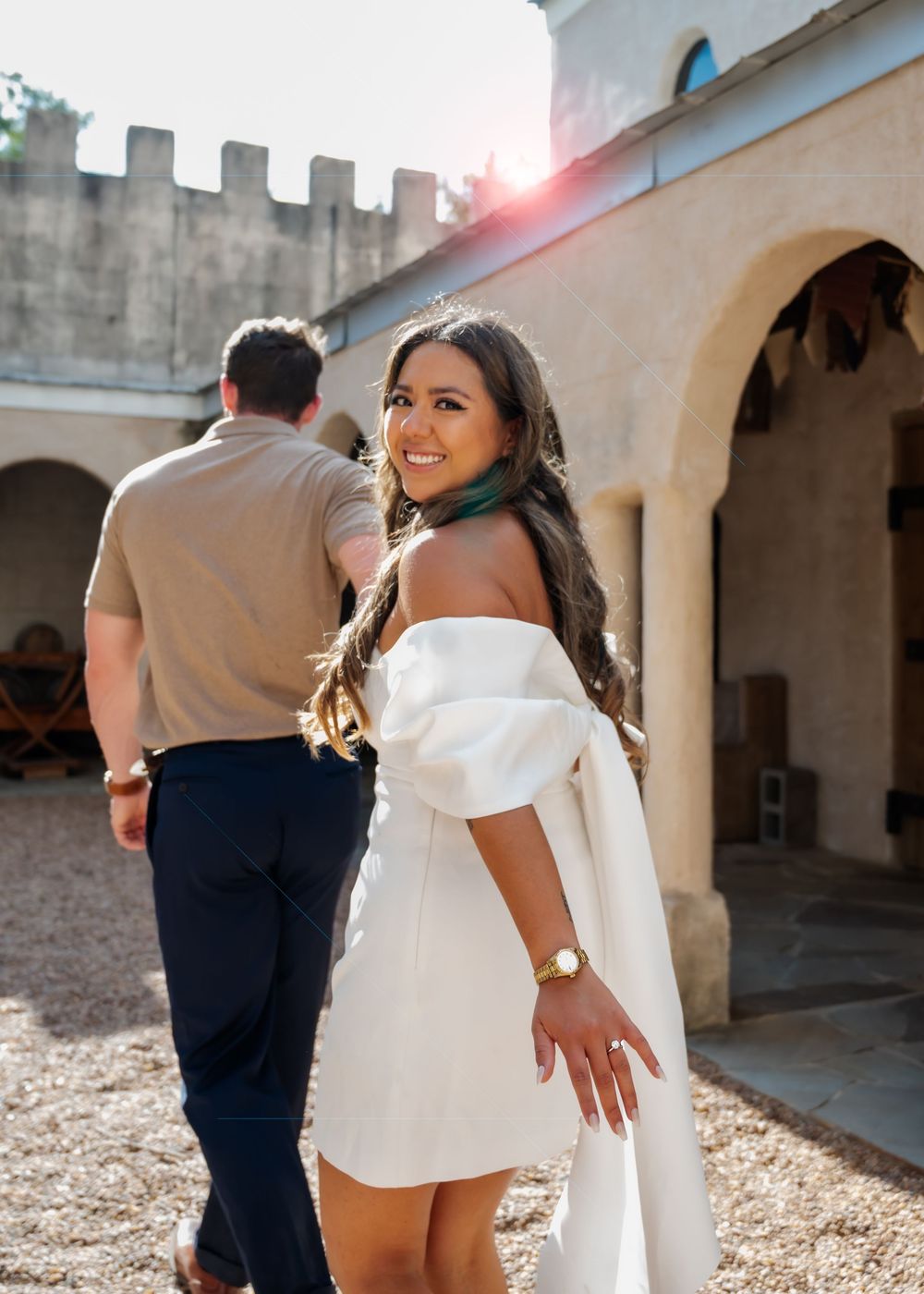 Smiling woman in white off-shoulder dress glances back at camera during golden hour.