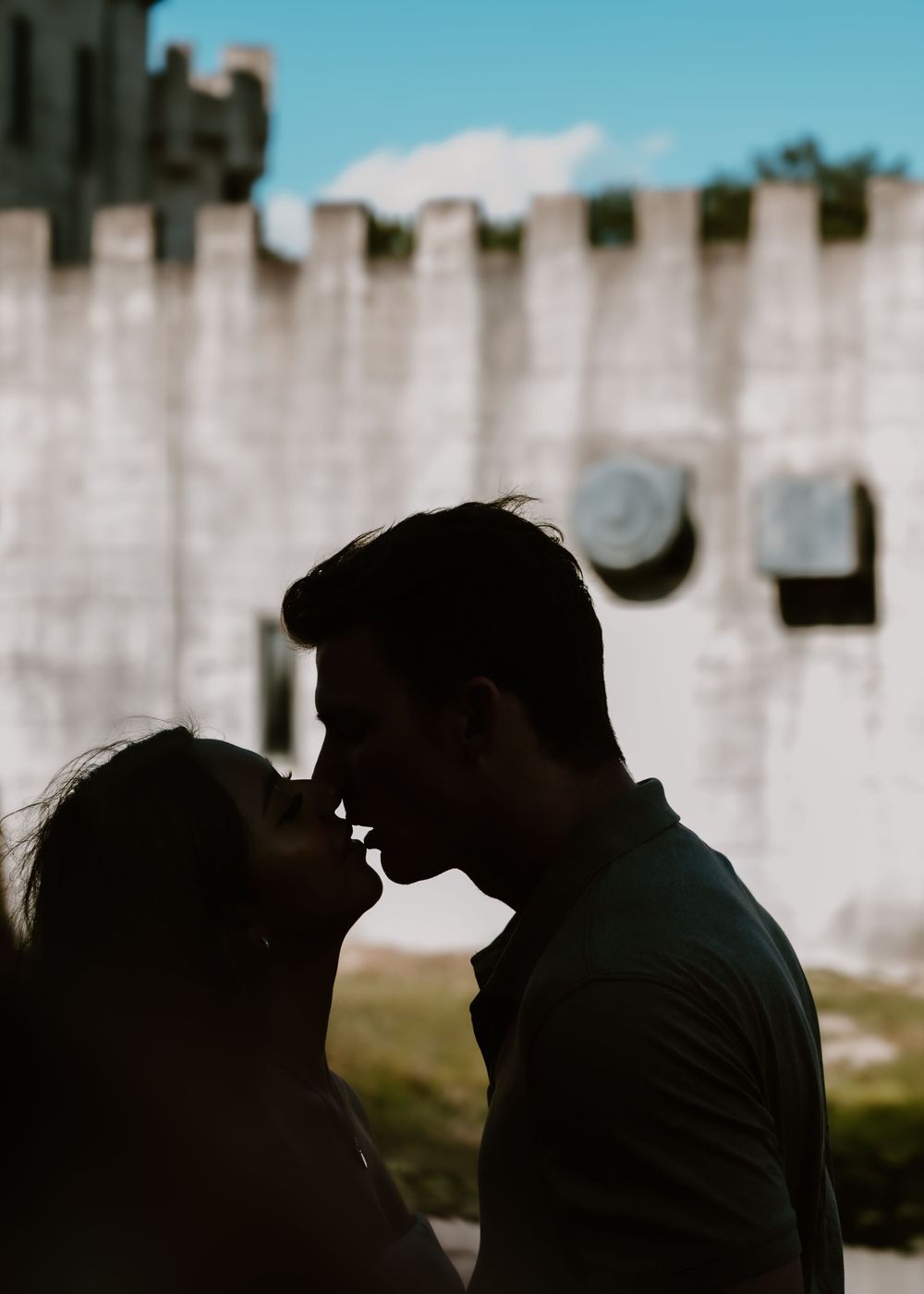Silhouette of couple sharing a kiss in front of ancient stone castle wall.