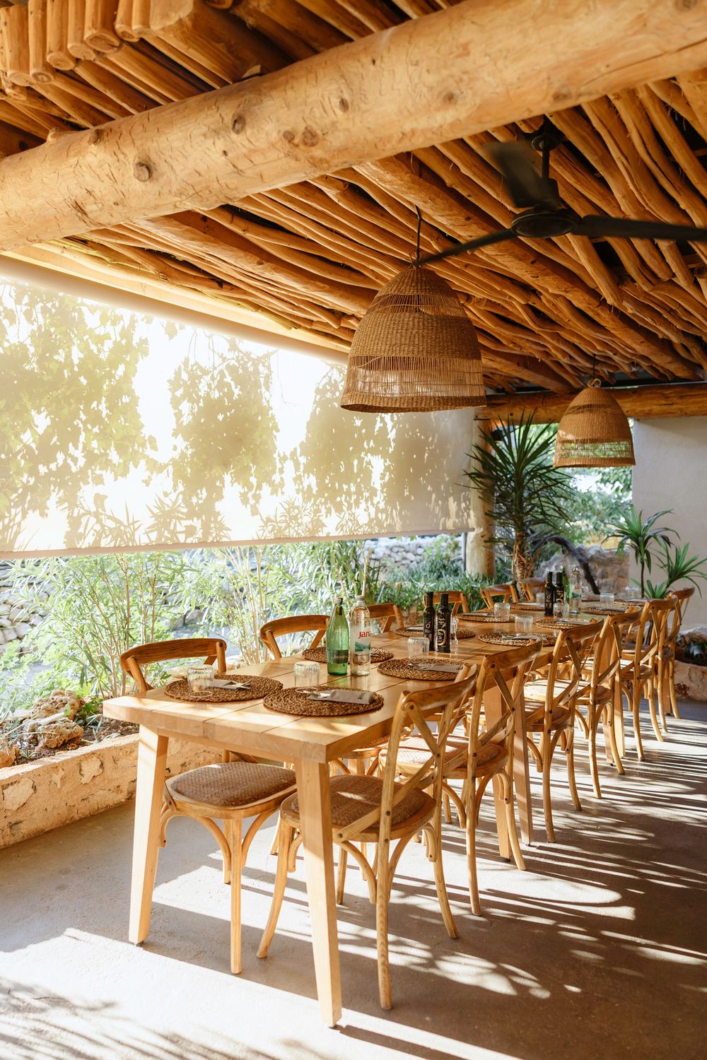 Rustic outdoor dining area with wooden tables and wicker pendant lights under a bamboo-covered patio overlooking greenery. Hvar, Croatia