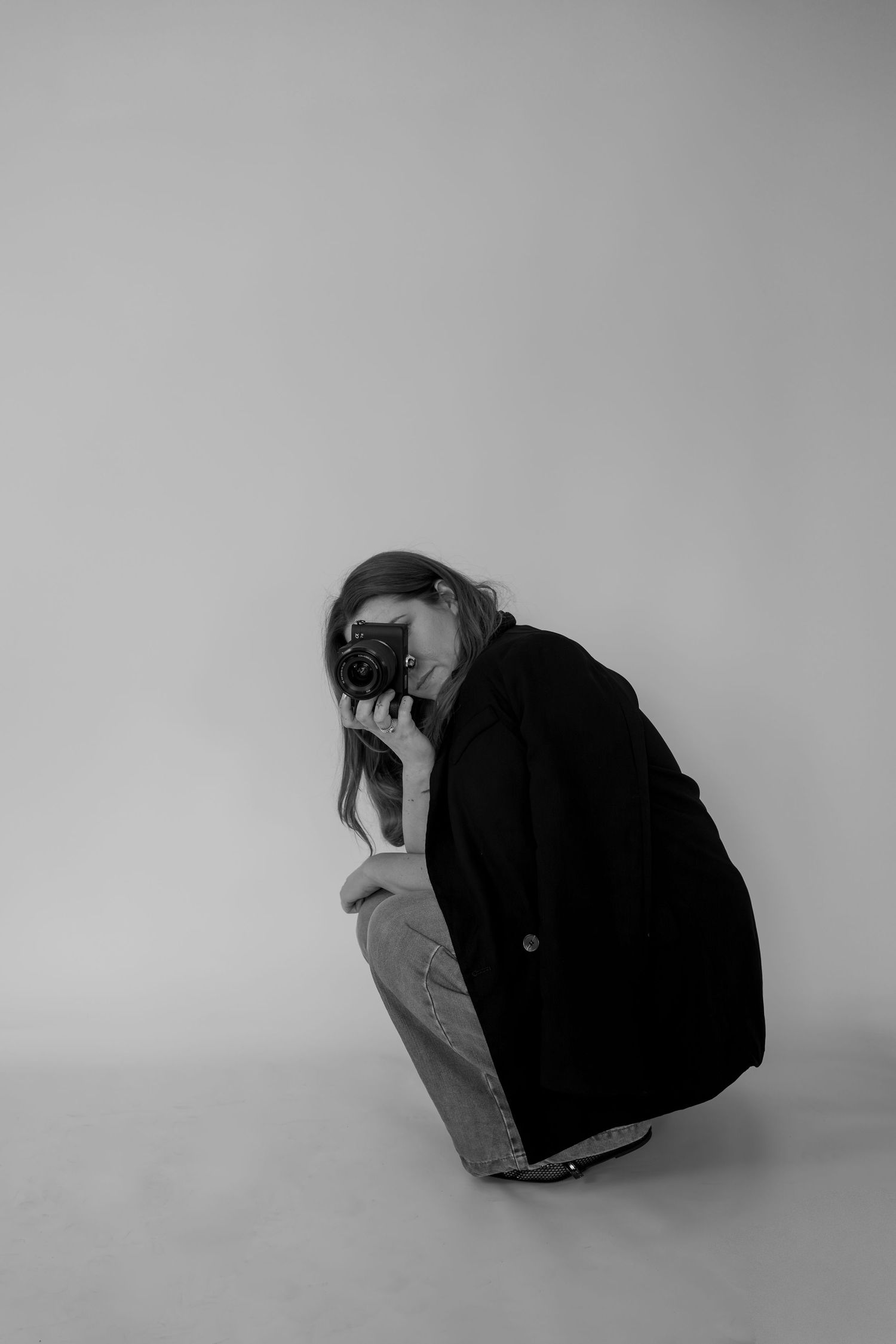 Woman in black sweater sits on brown leather couch holding professional camera.