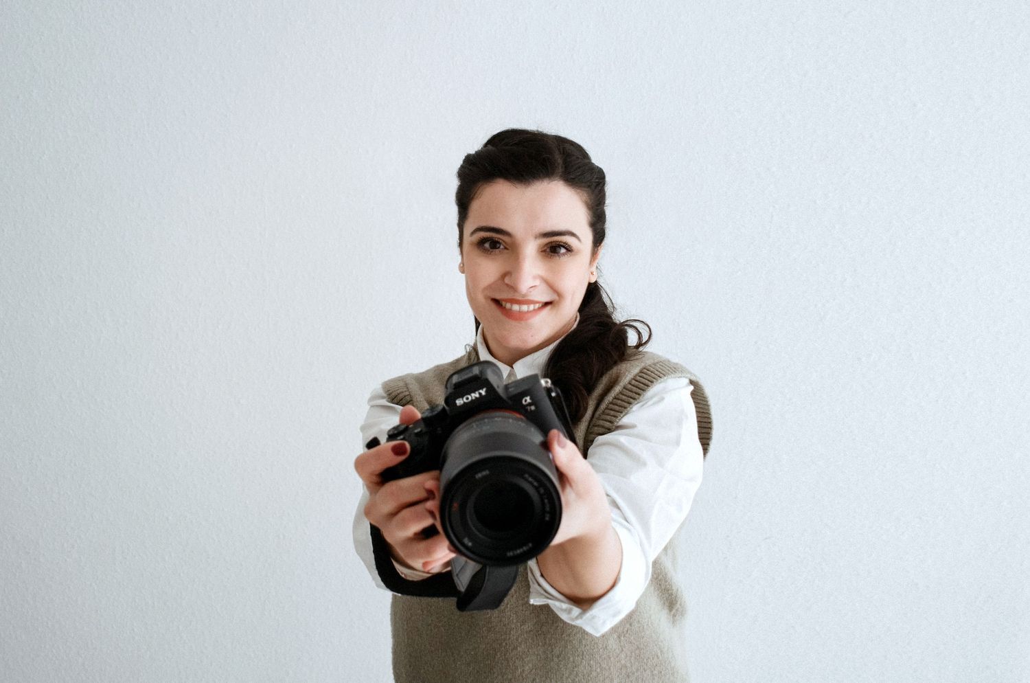 Professional photographer in white sweater holding camera against light background.