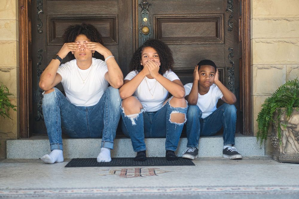 Family of three sitting on steps making playful see-no-evil poses together.