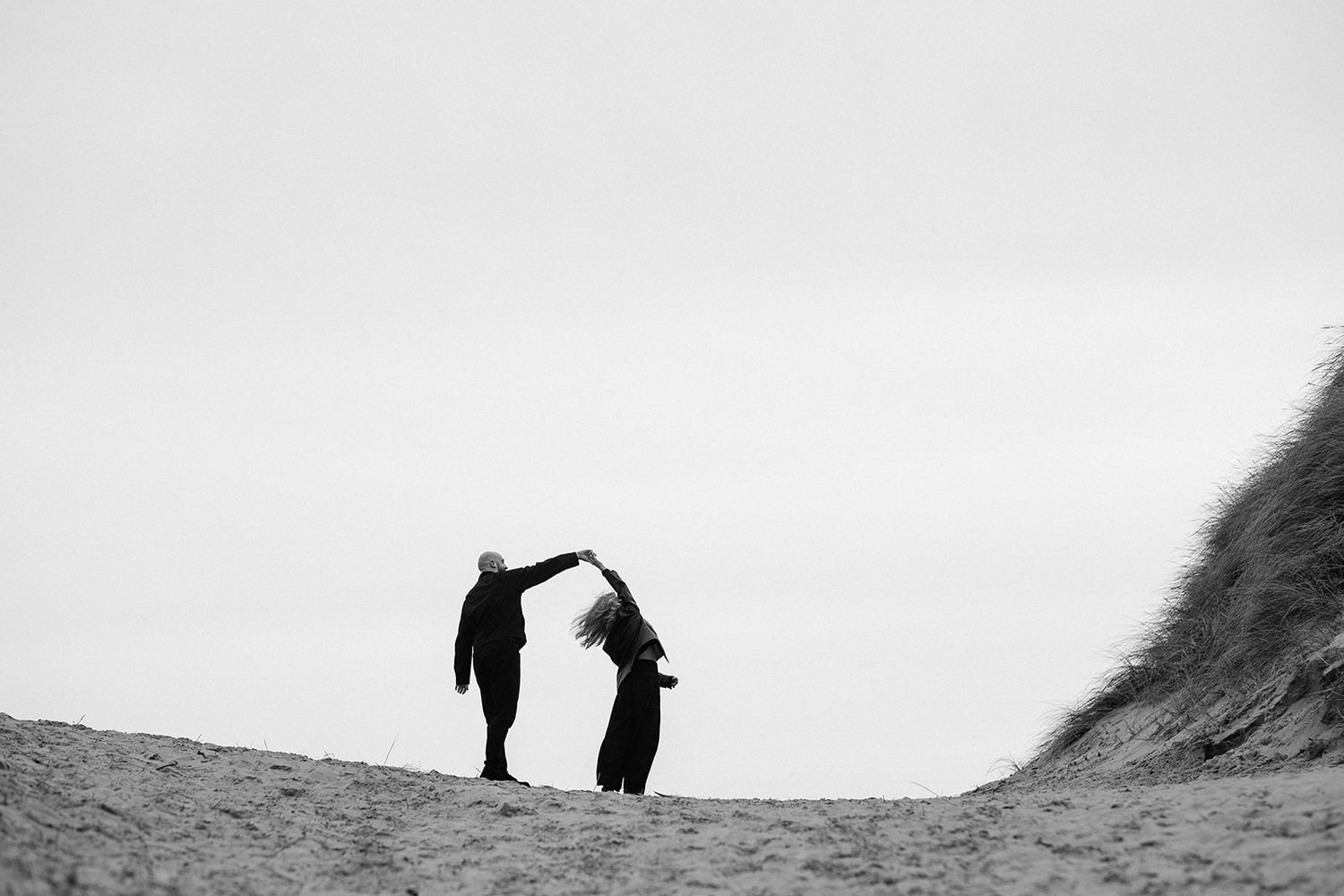 Two people dancing on a sandy dune in a black and white outdoor photo.