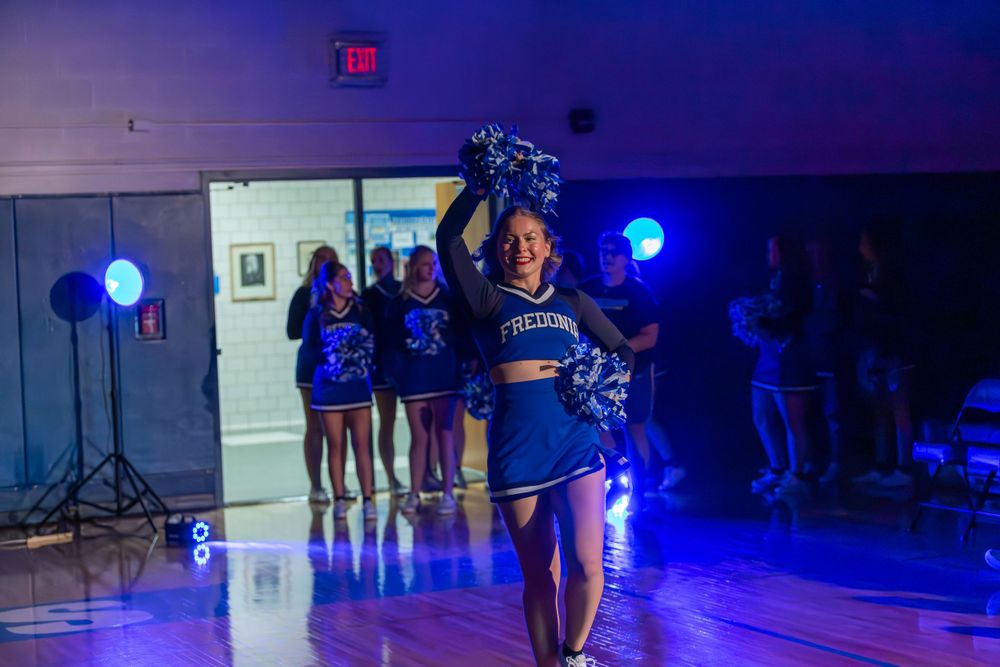 Athletes in uniform walking through a gymnasium illuminated by blue spotlights.