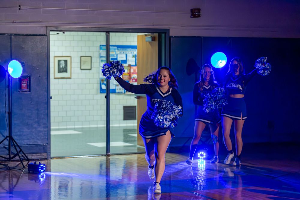 Performers entering through gymnasium doors under atmospheric blue stage lighting.