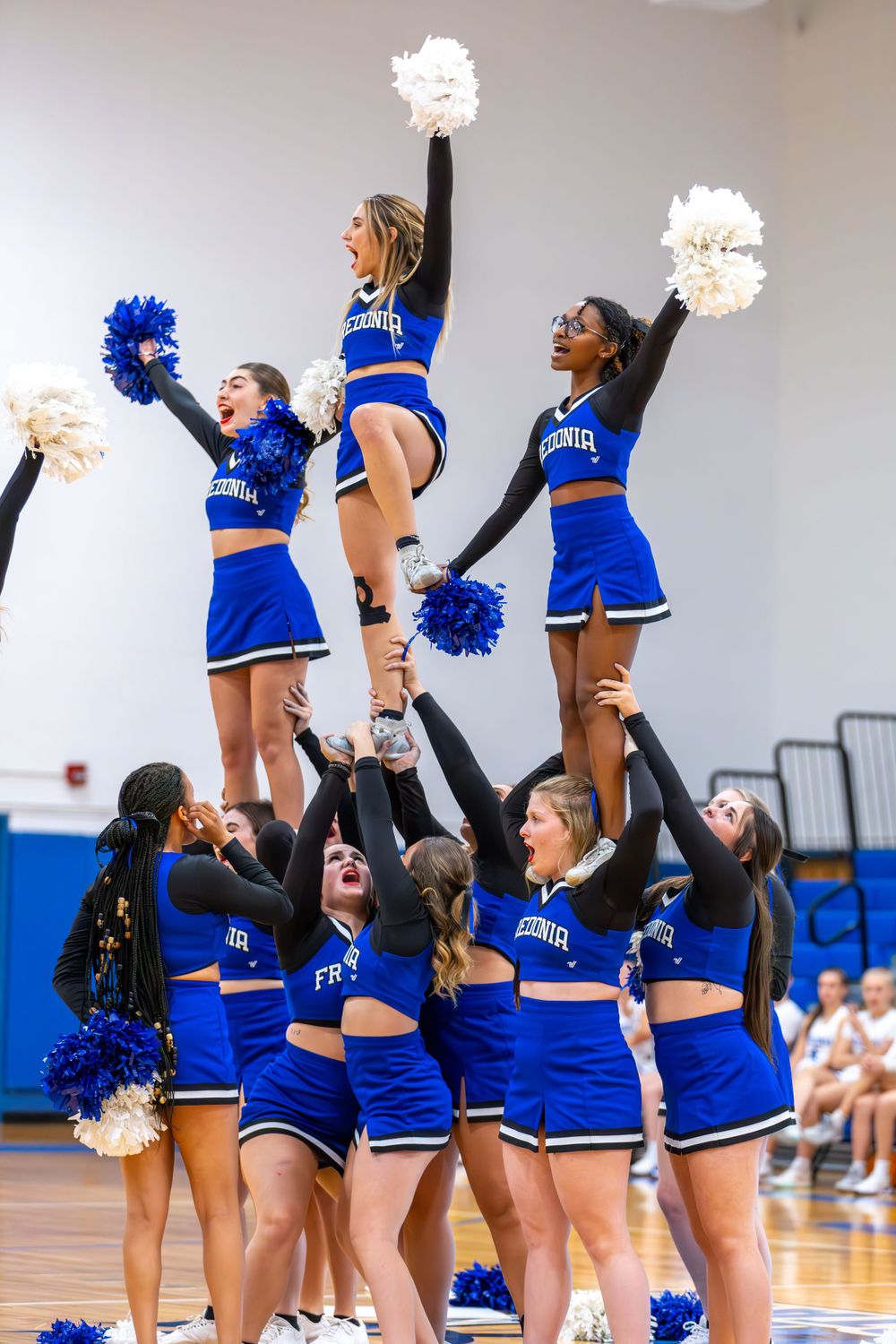 Cheerleaders in blue uniforms perform synchronized routines during an indoor sports event.