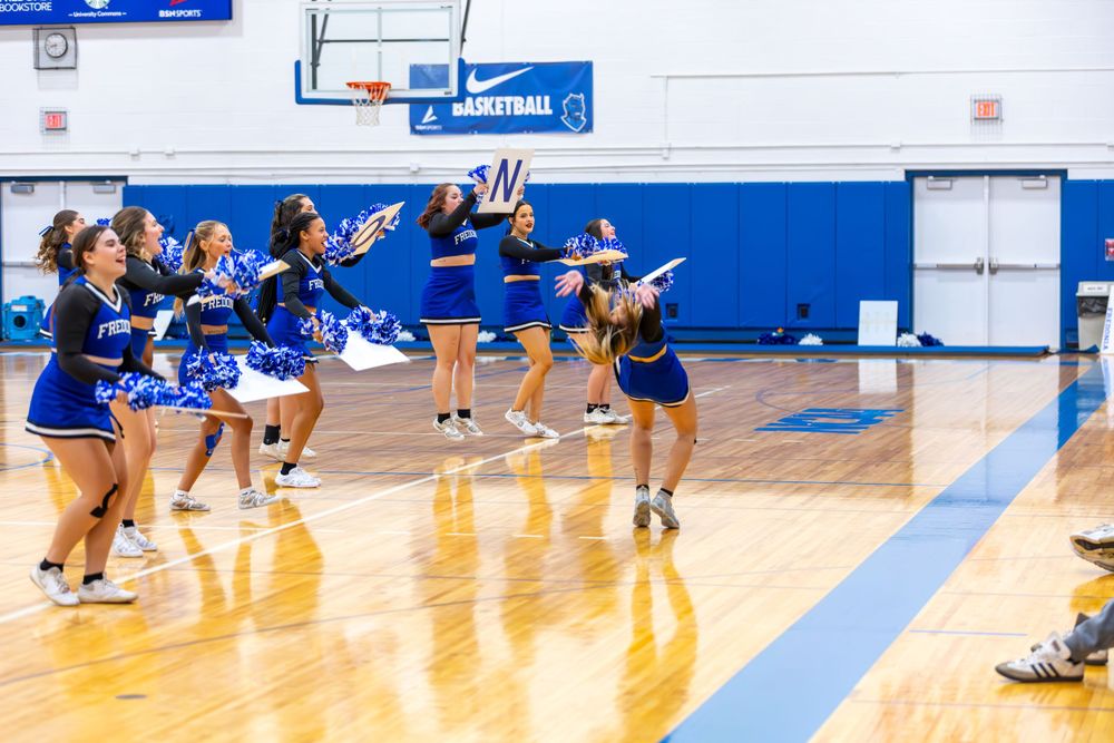 Cheerleaders perform energetic formations on a blue and white gymnasium floor.