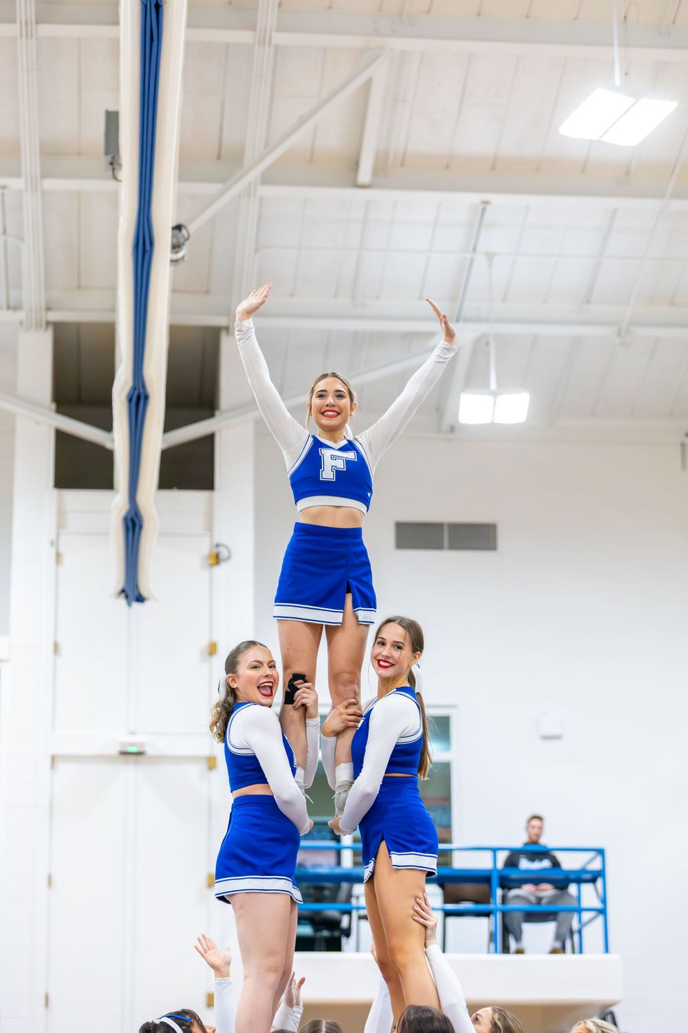 Cheerleaders execute a liberty stunt formation in blue and white uniforms.