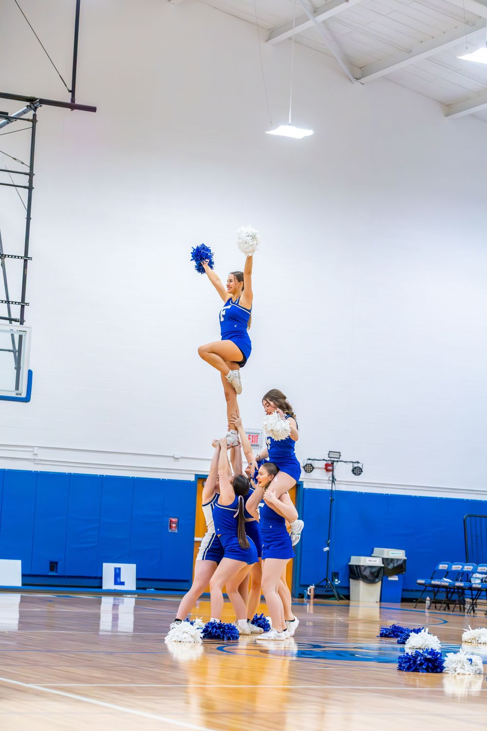Cheerleaders perform a high-flying stunt formation in blue uniforms during a basketball game.