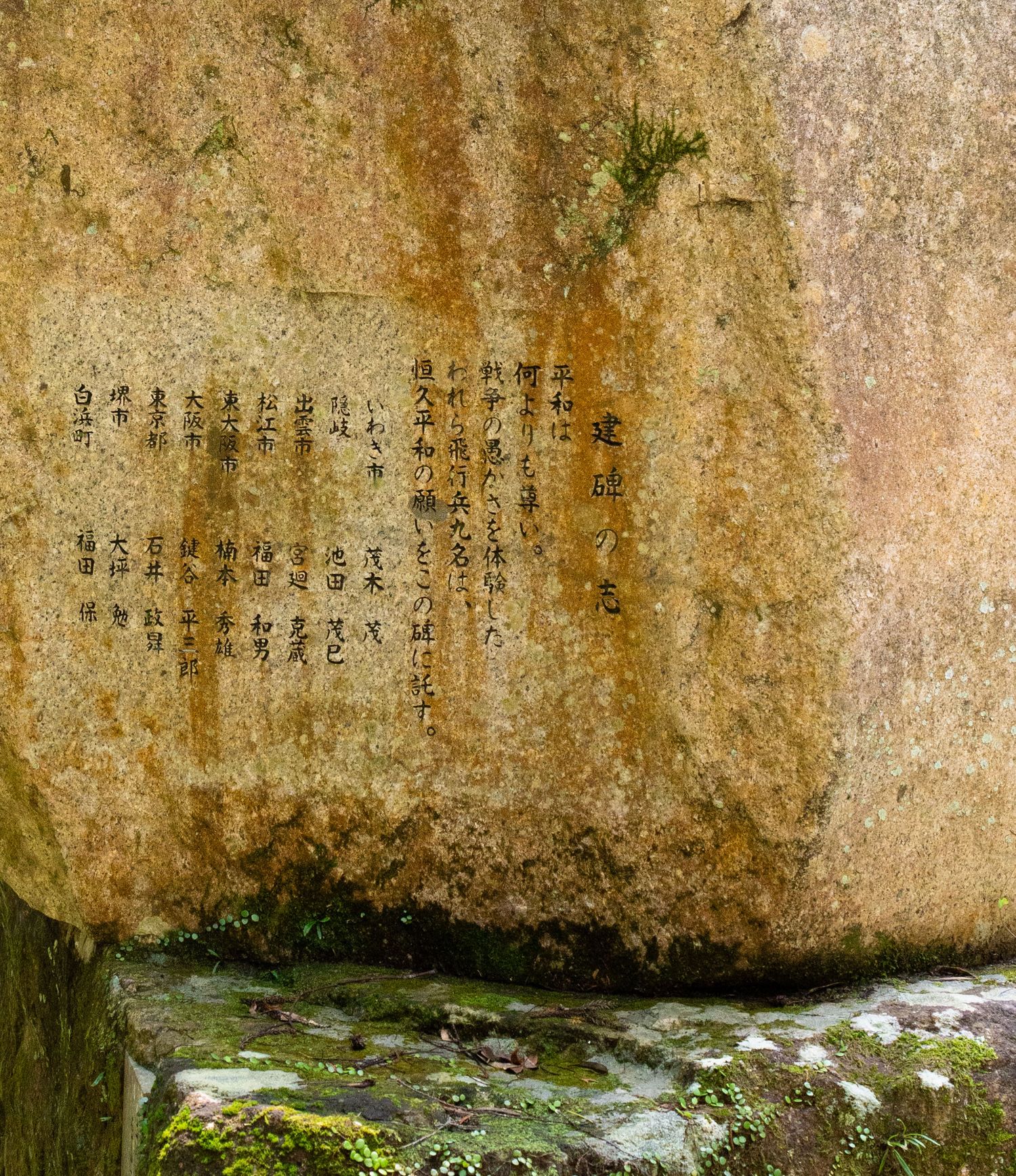 Ancient stone wall with carved Chinese characters and moss growing on its surface.