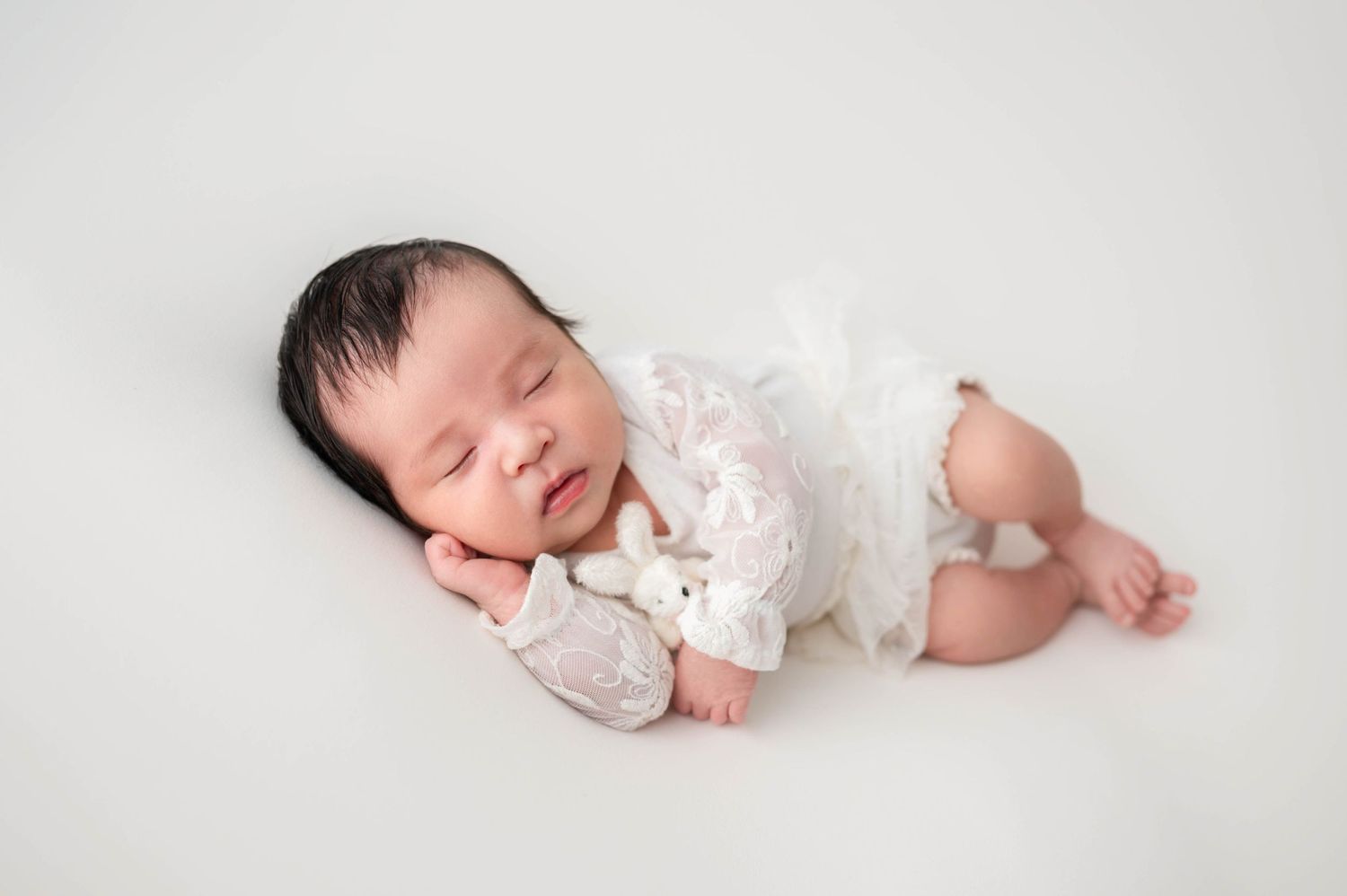 Peaceful newborn sleeping in soft white blanket during luxury photography session in Woodbury, MN