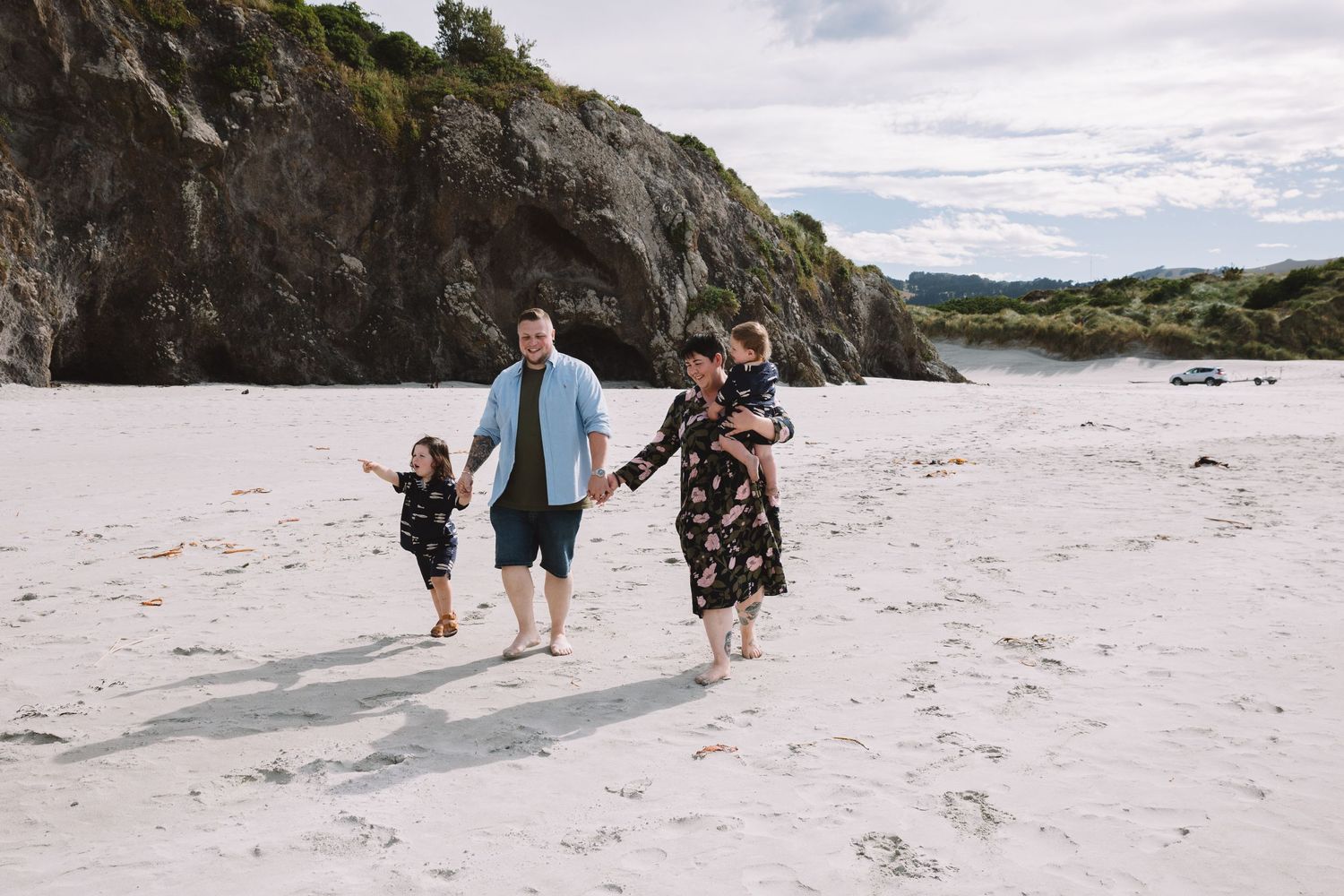 Family walking together holding hands on a pristine white sand beach with rocky cliffs.