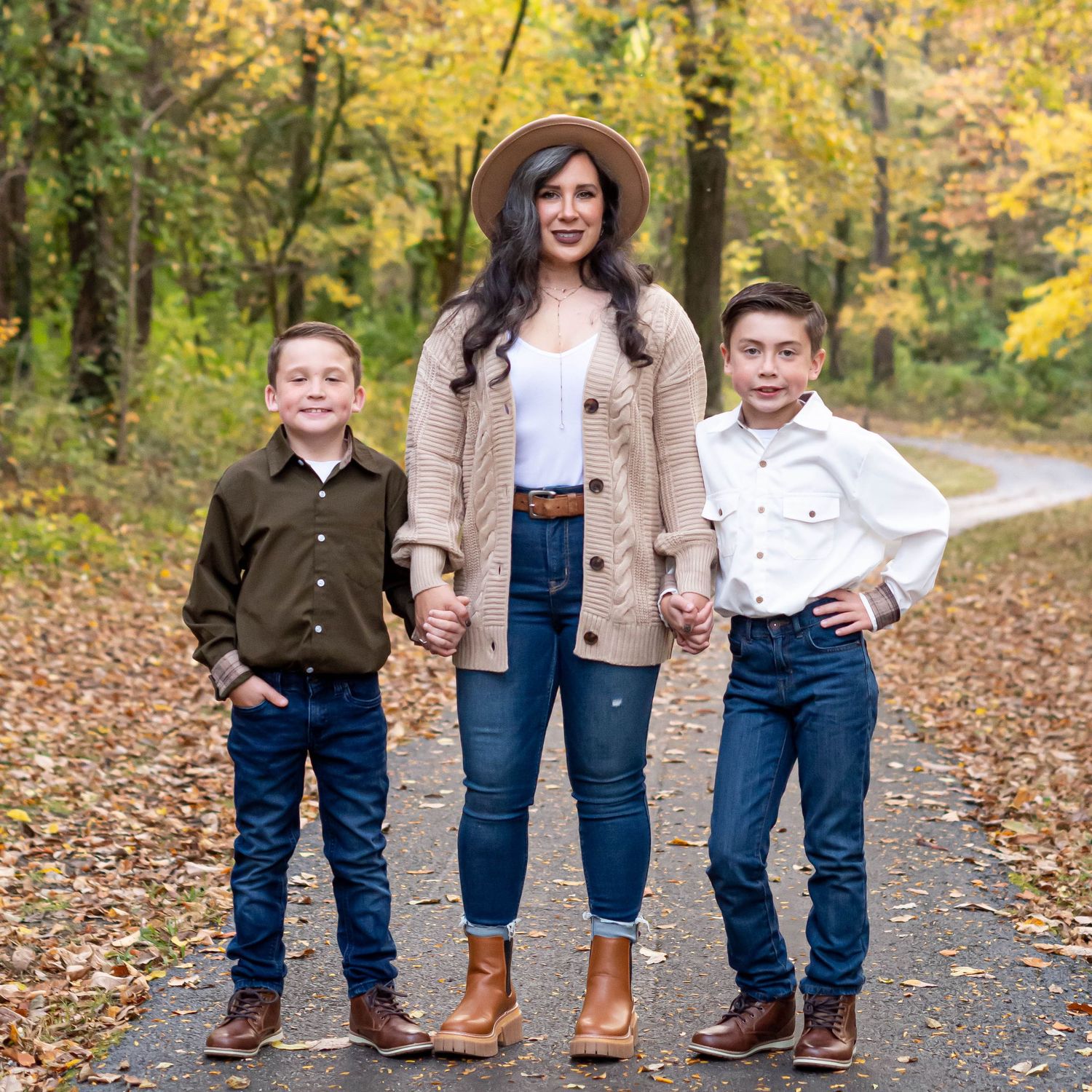 Three people pose on a leaf-covered path surrounded by golden autumn trees.