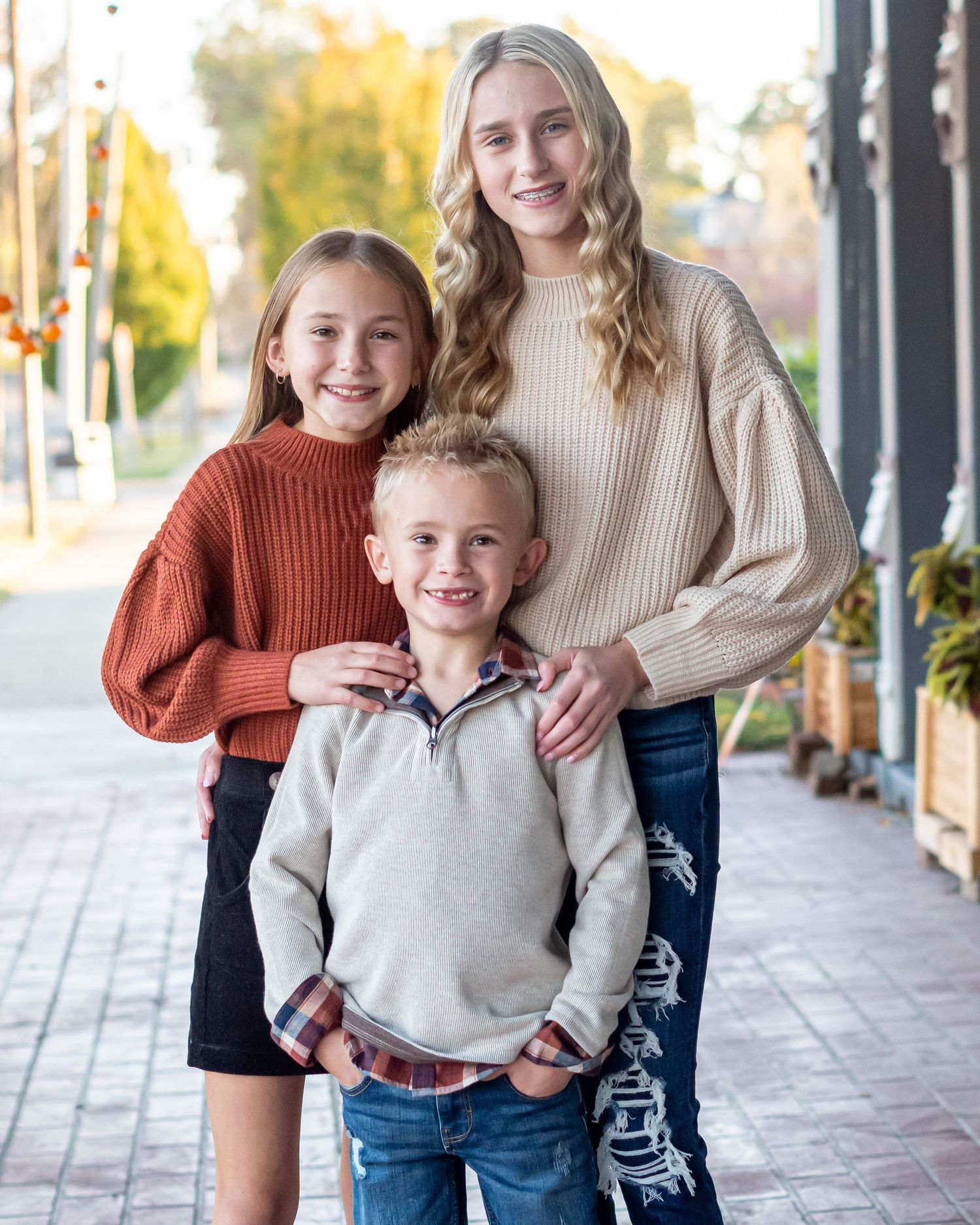 Three people in cozy sweaters pose together on a downtown sidewalk during autumn.
