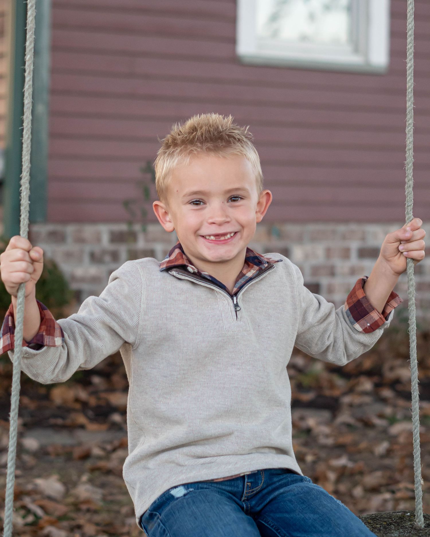 Young boy in grey sweater smiling while sitting on a swing.