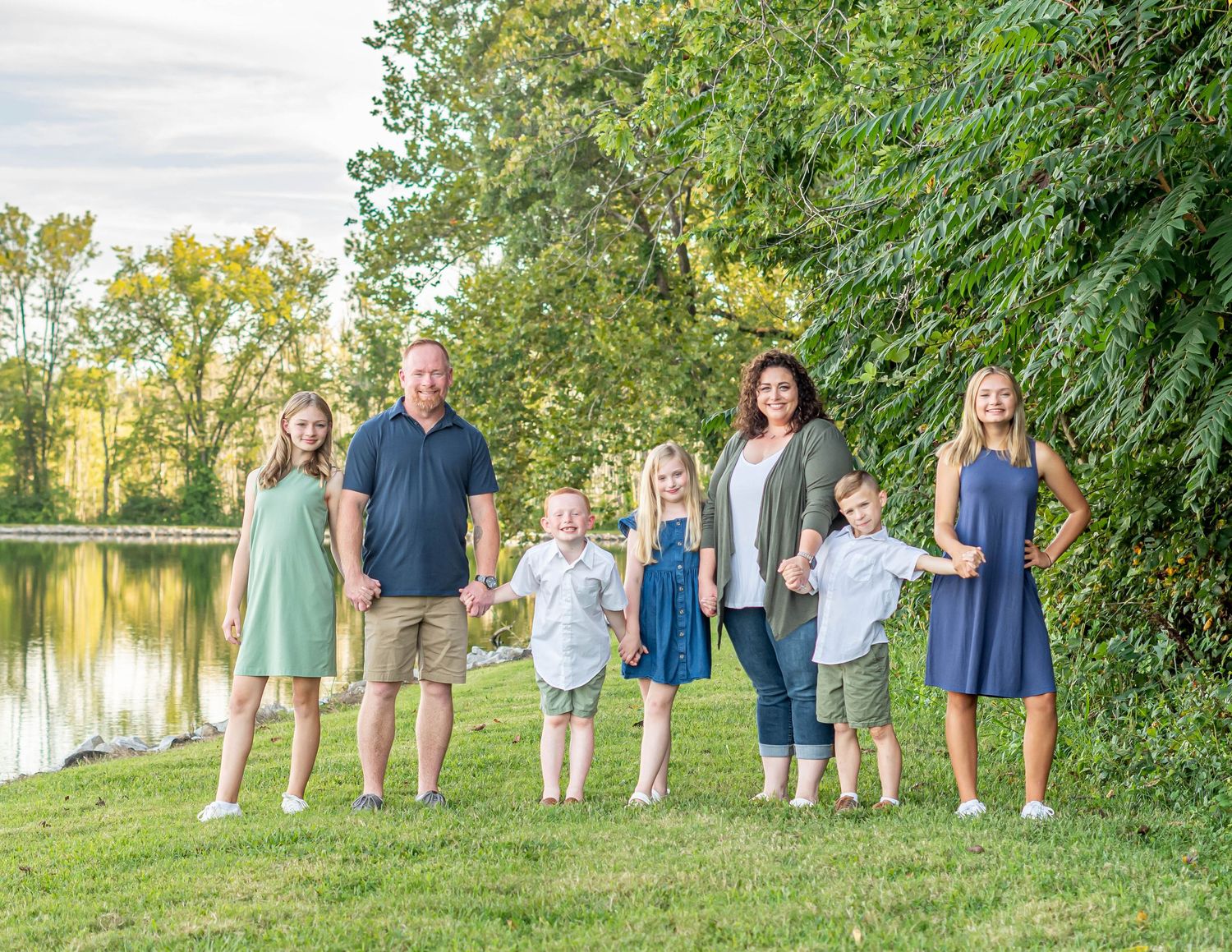 Family group poses together by lake with trees and water in summer setting.