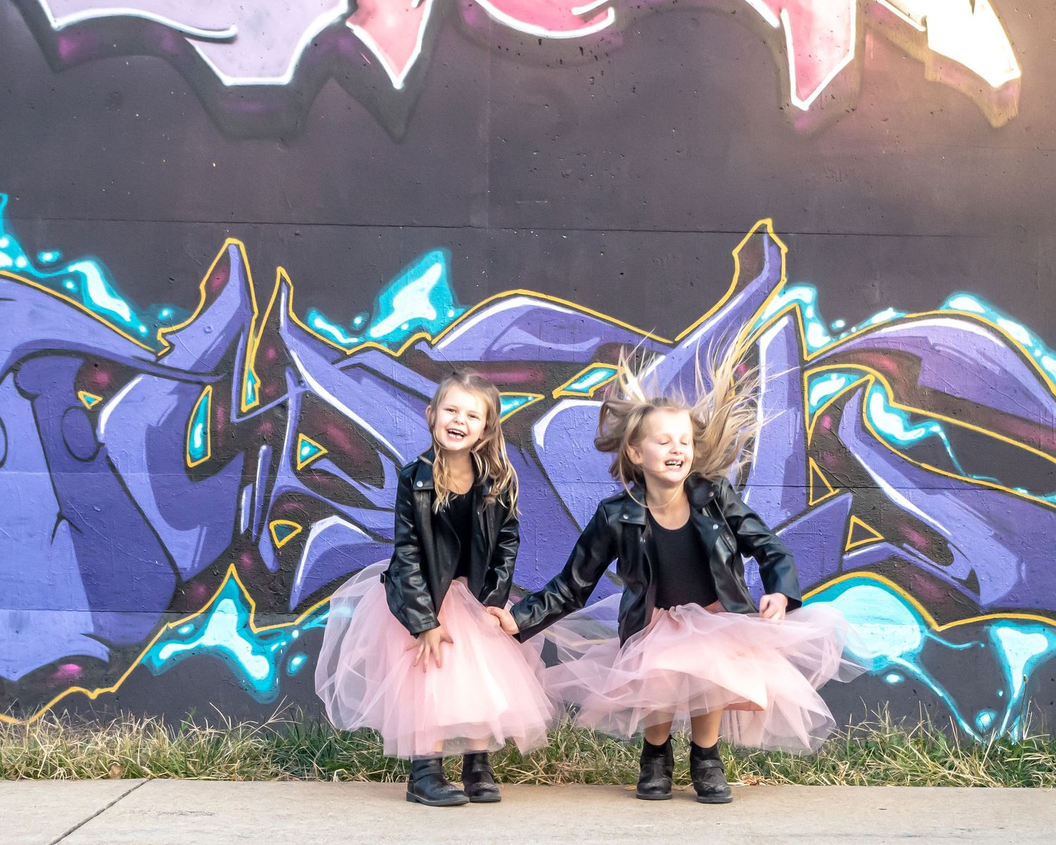Two people in matching outfits jump in front of blue graffiti wall.