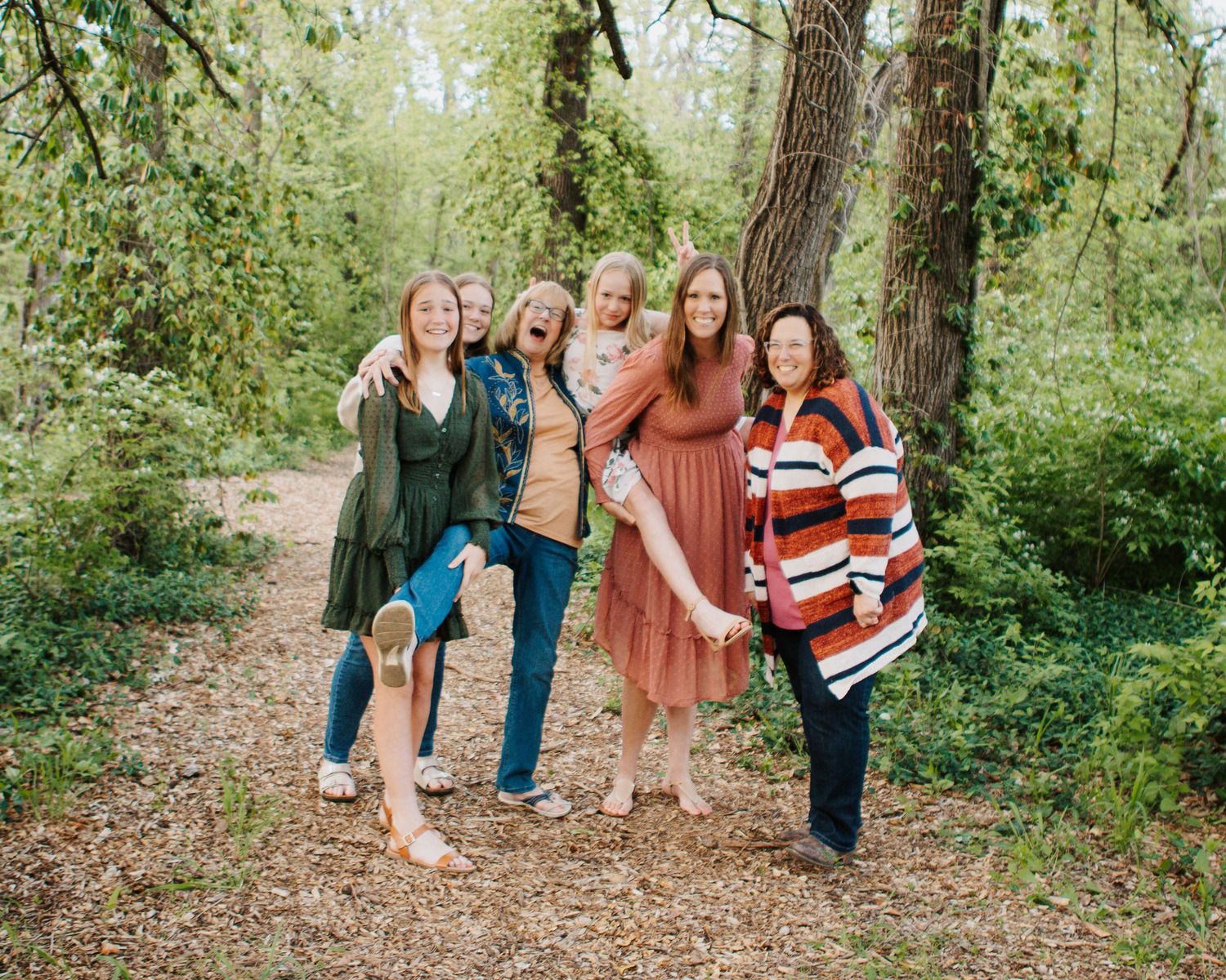 Group of friends pose together on wooded trail in casual fall outfits.