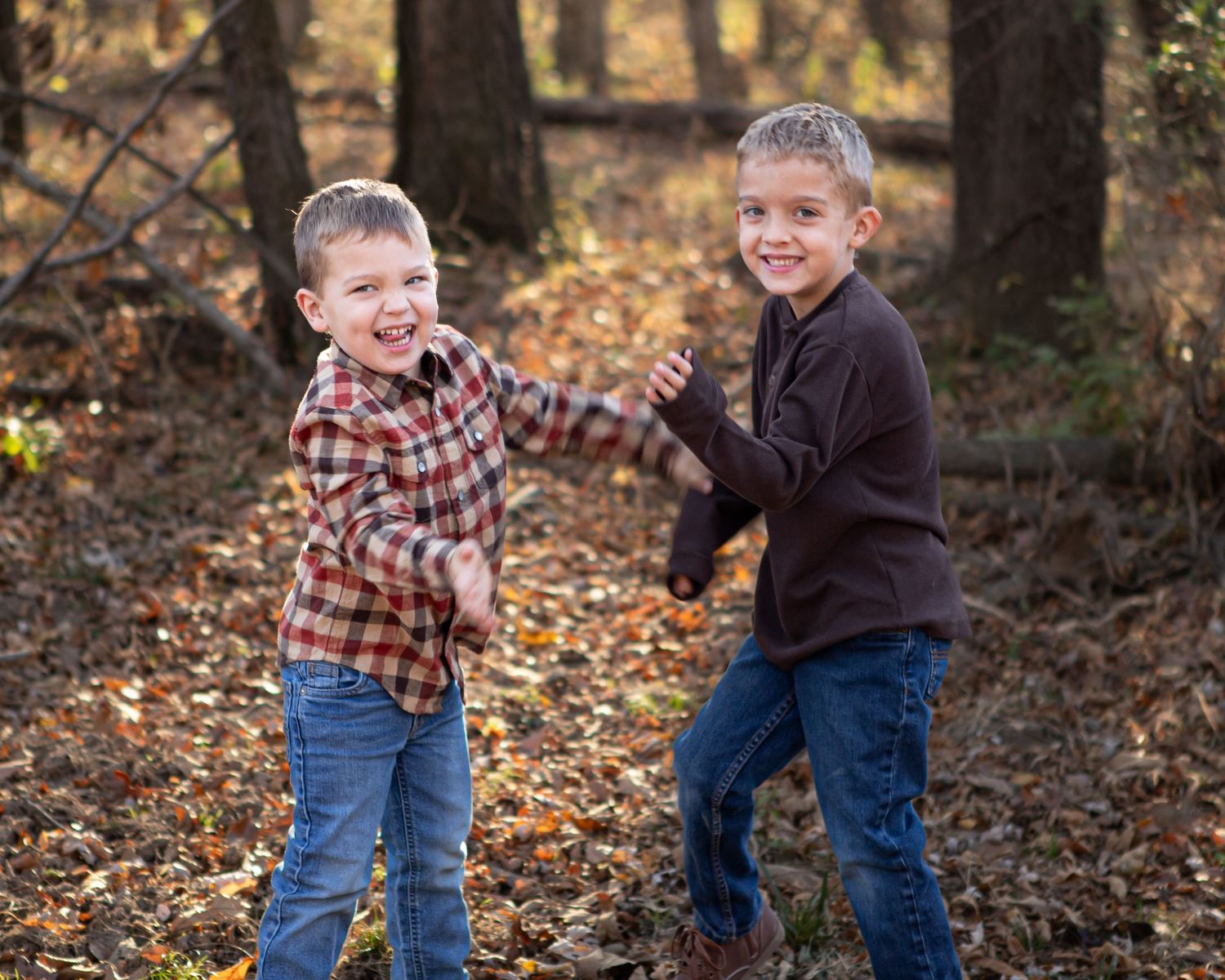 Two young boys play and laugh together in autumn forest setting.