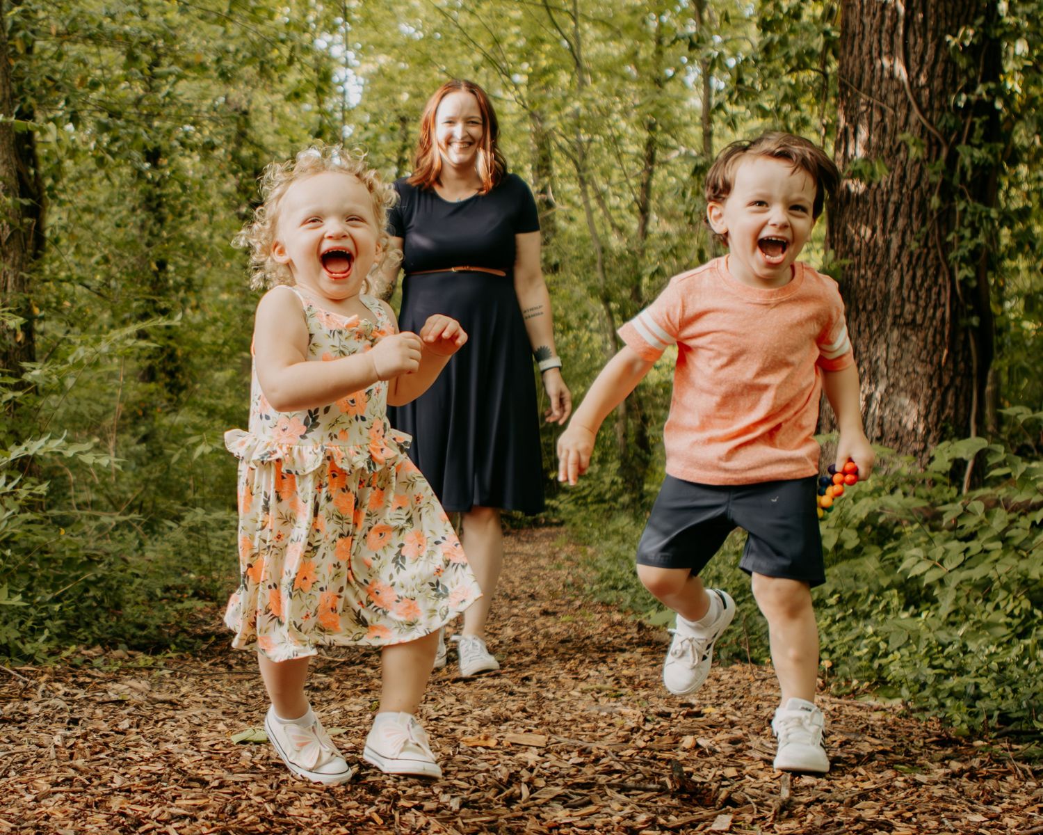 Children playing and laughing together on a wooded trail covered in fallen leaves.