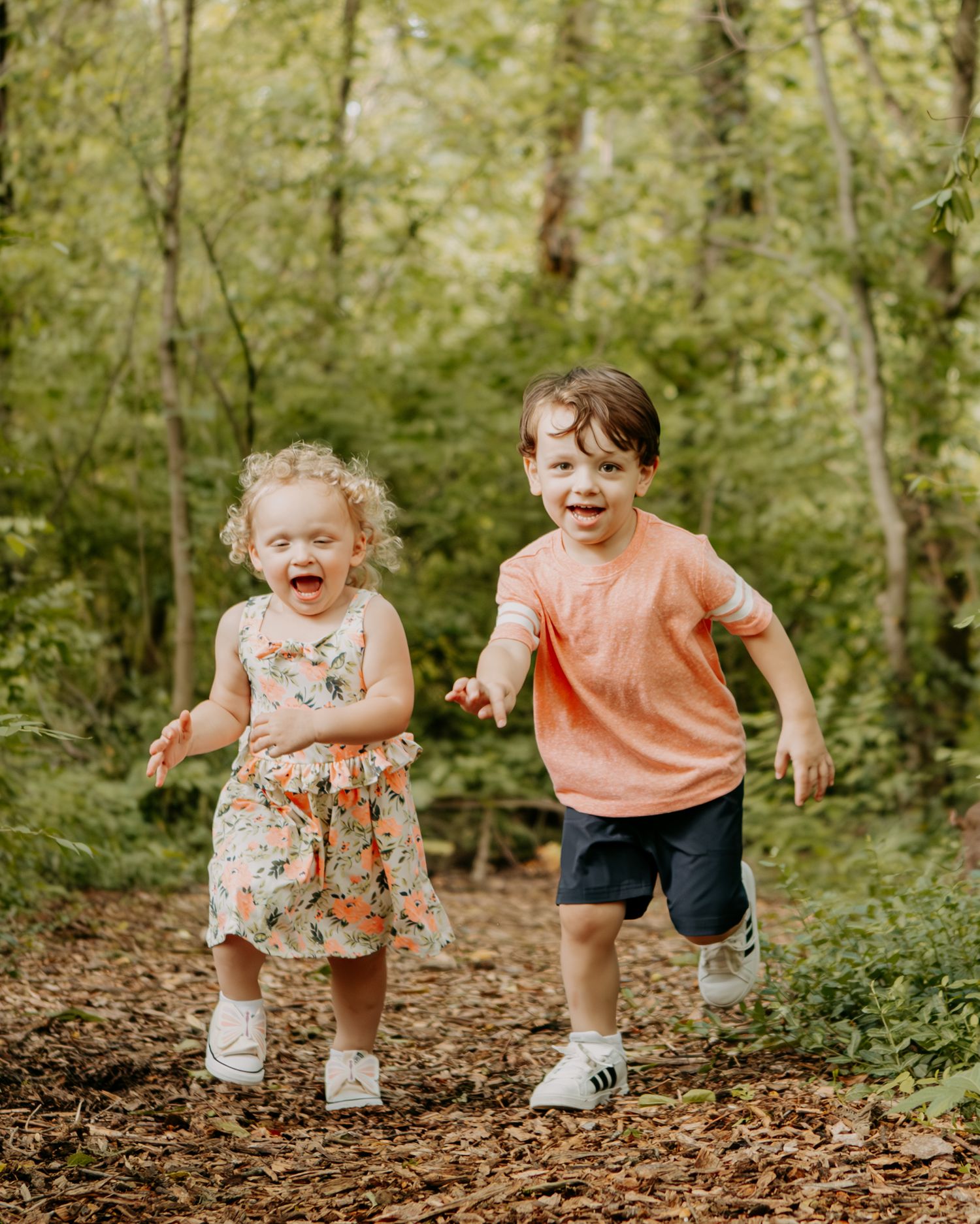 Children running and playing together on a leaf-covered forest path.
