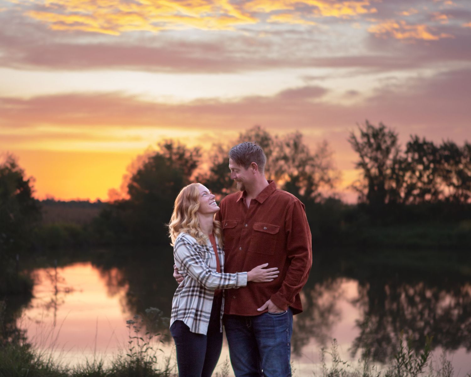 Romantic couple embracing during golden hour by a serene lake.