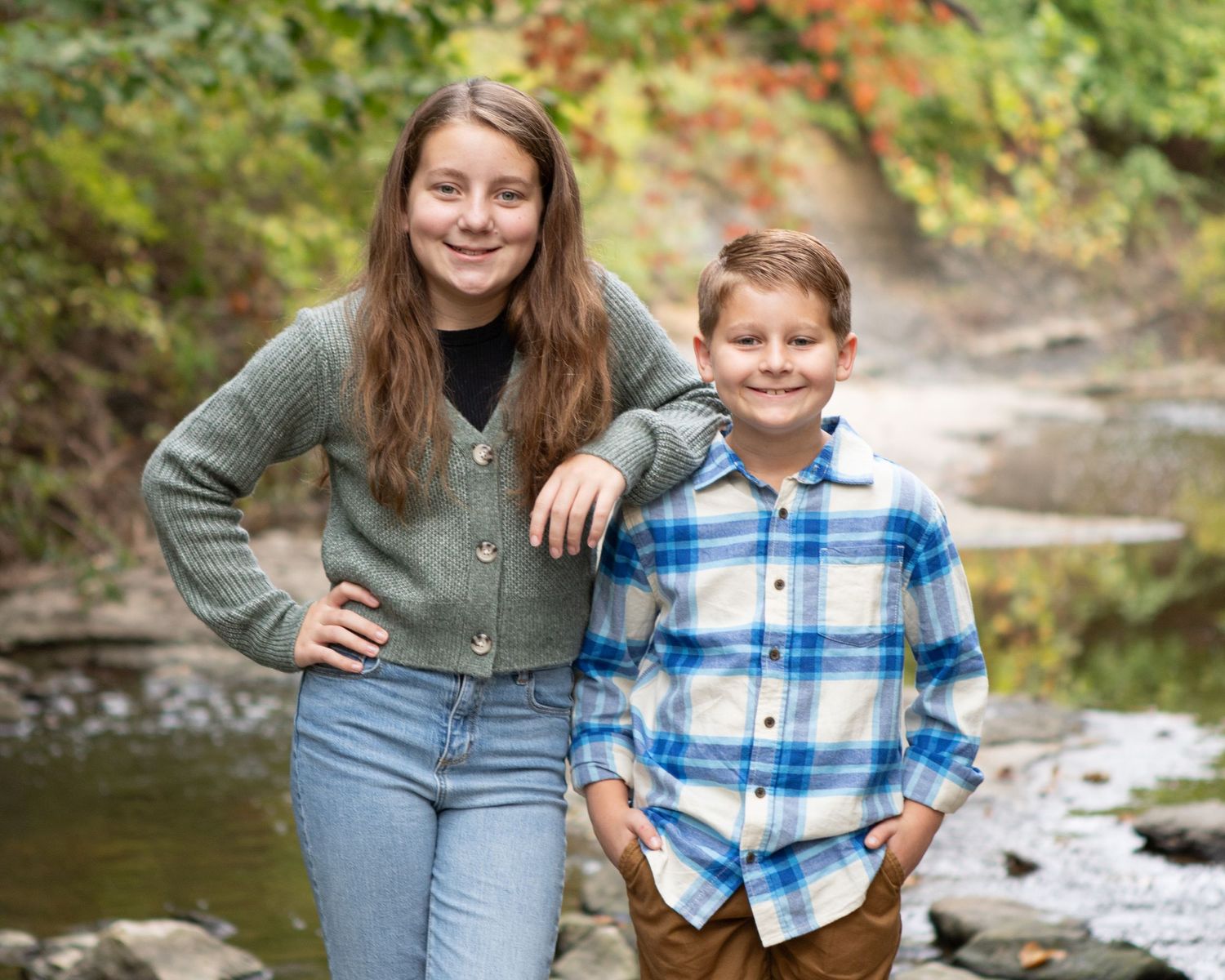 A family poses together on rocks near a stream surrounded by autumn foliage.