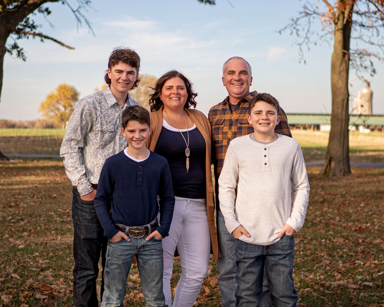 A group poses together outdoors during autumn with trees in the background.