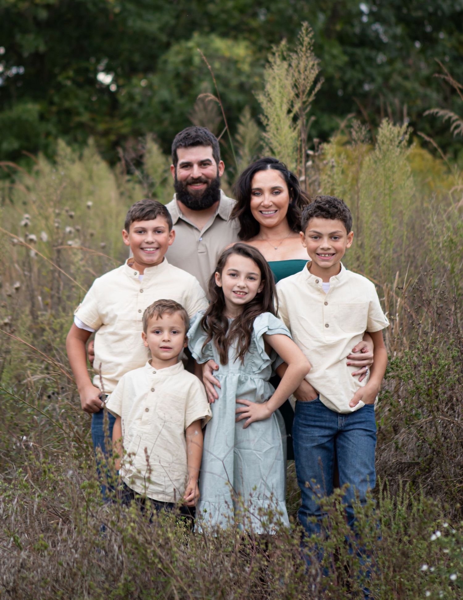 A family wearing coordinated outfits poses together in a field of tall grass.