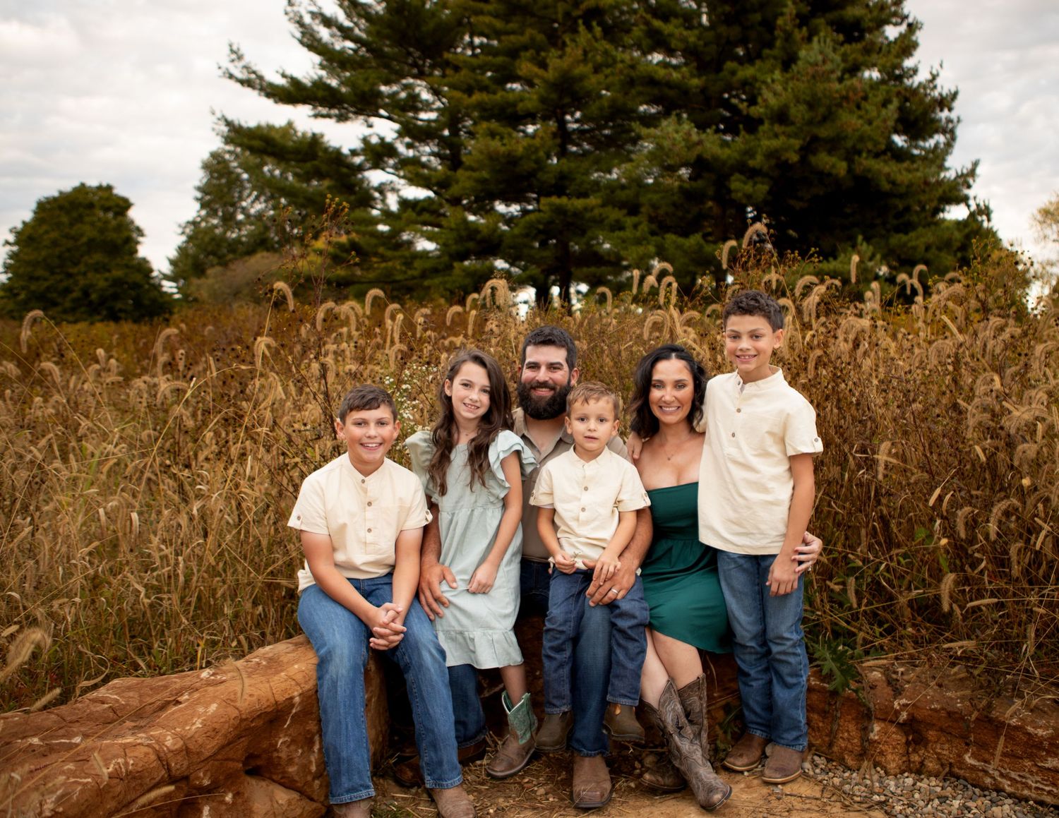 A family group sits together on a fallen tree trunk in an autumn landscape.