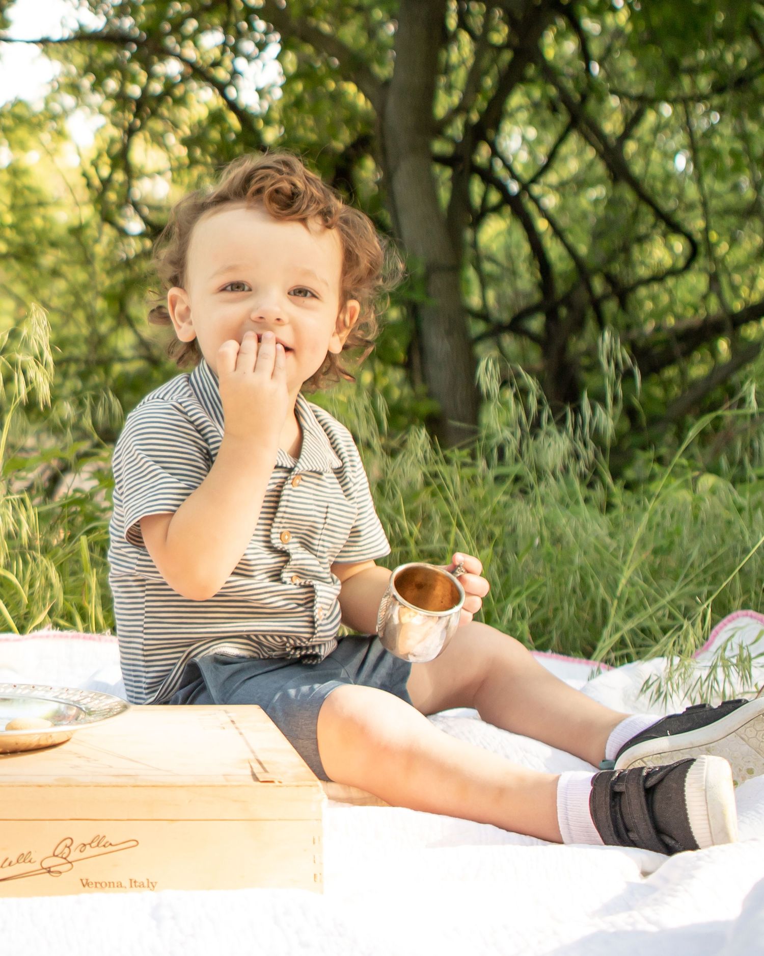 A young child having a snack outdoors while sitting on a picnic blanket.