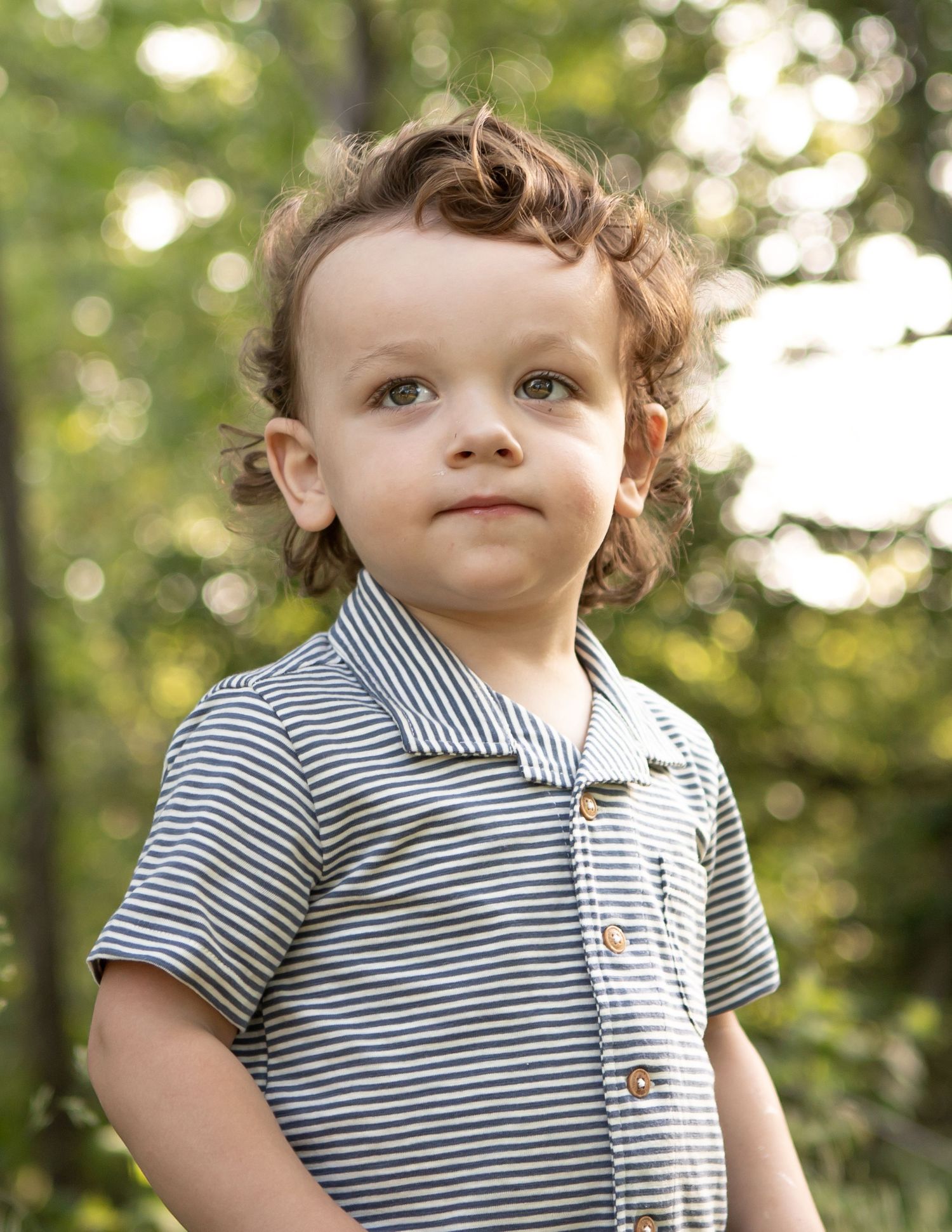 Close up of a toddler in striped polo shirt outdoors with bokeh background.
