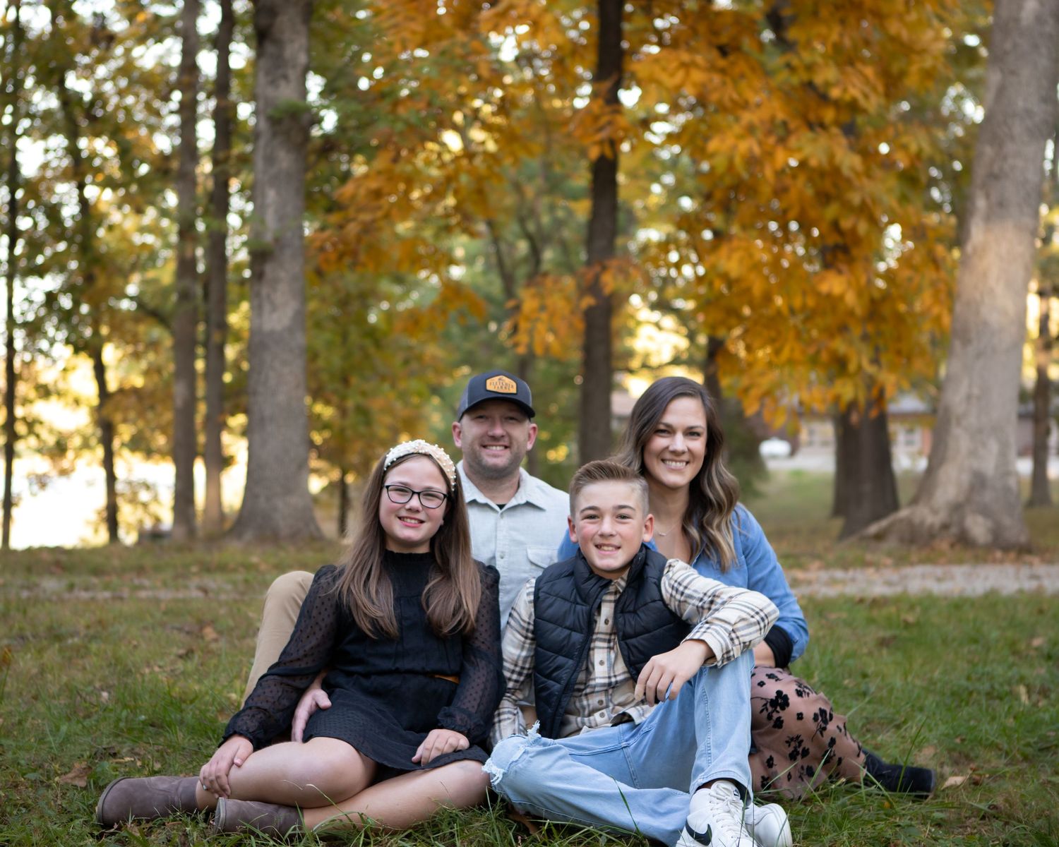 Family of four poses together on grass during autumn with golden trees in background.