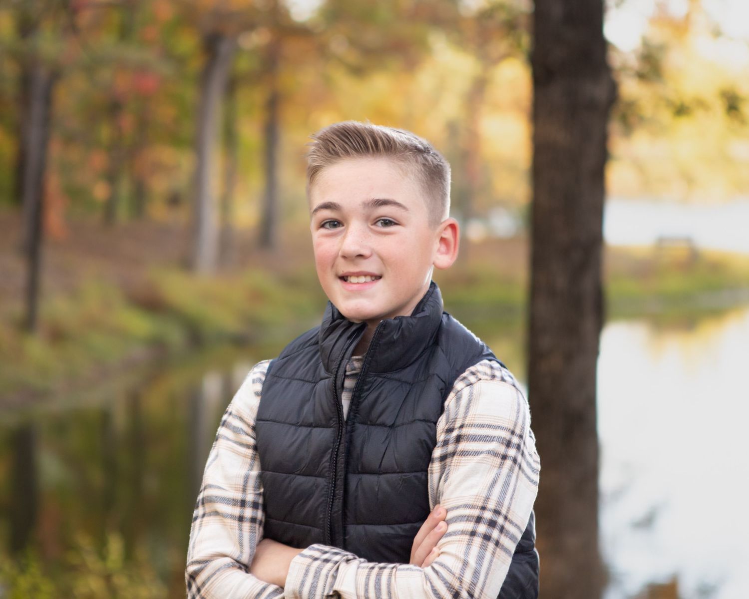 Portrait of youth in plaid shirt and black vest against fall foliage.