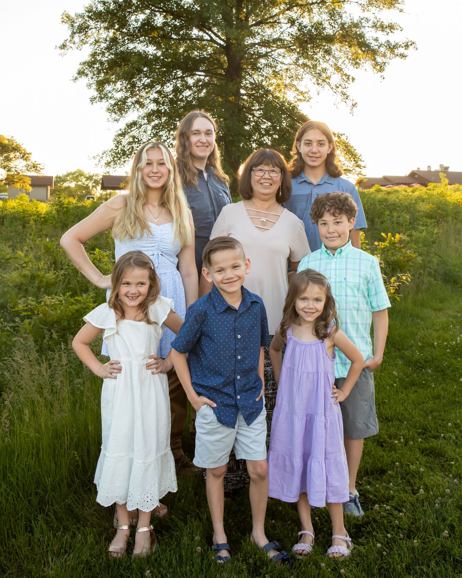 Group portrait of seven people in coordinated outfits standing together in sunlit field.